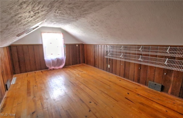 bonus room with a textured ceiling, wood walls, vaulted ceiling, and light hardwood / wood-style flooring