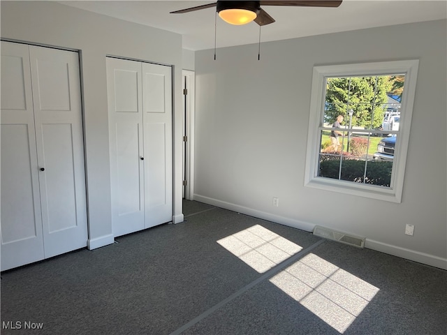 unfurnished bedroom featuring ceiling fan, dark colored carpet, and two closets