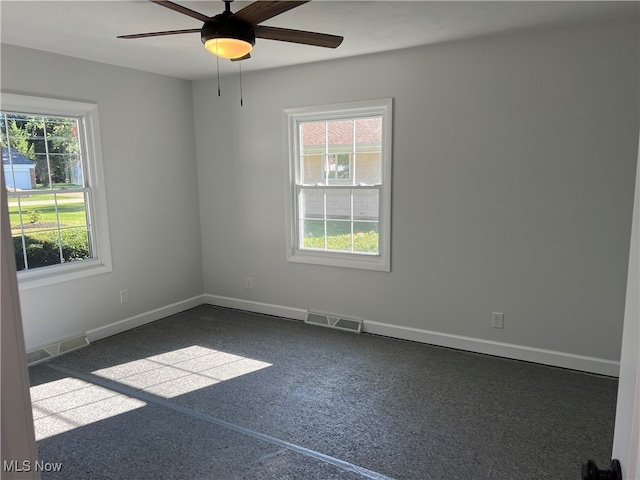 spare room with a wealth of natural light, dark carpet, and ceiling fan