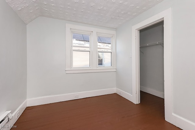 unfurnished bedroom featuring a textured ceiling, lofted ceiling, dark hardwood / wood-style floors, and a closet