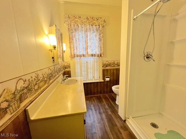 bathroom featuring walk in shower, vanity, hardwood / wood-style floors, toilet, and wood walls