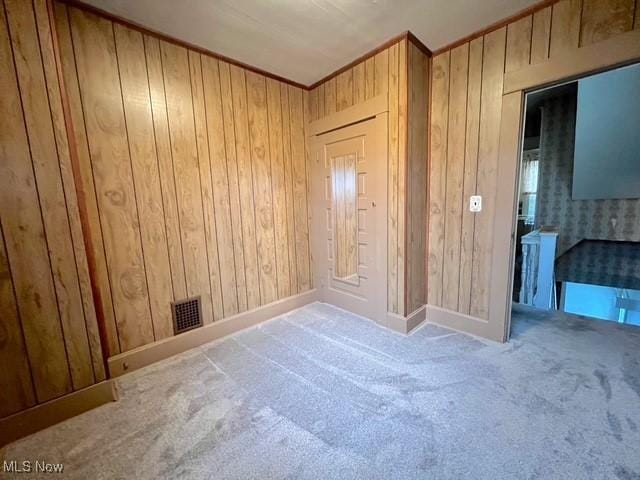 carpeted empty room featuring wood walls