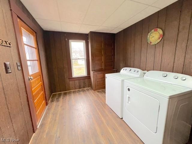 laundry area with wood walls, washing machine and dryer, and light wood-type flooring