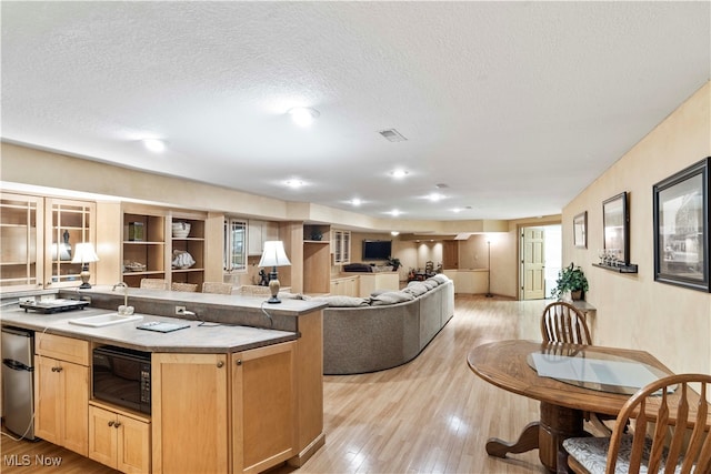 kitchen featuring light wood-type flooring, a textured ceiling, sink, black microwave, and light brown cabinetry