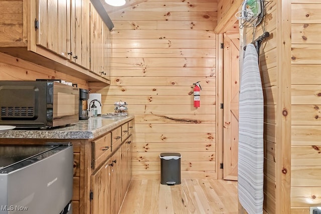 kitchen with light wood-type flooring, wooden walls, light brown cabinets, and sink