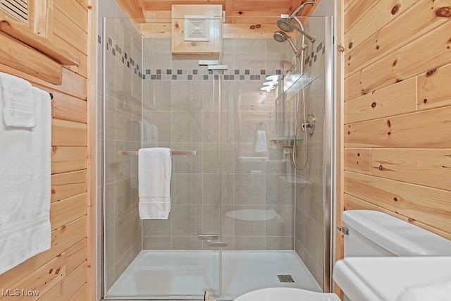 bathroom with wood walls, toilet, and a shower with shower door