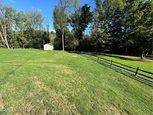 view of yard featuring a storage shed, a rural view, an outdoor structure, and fence