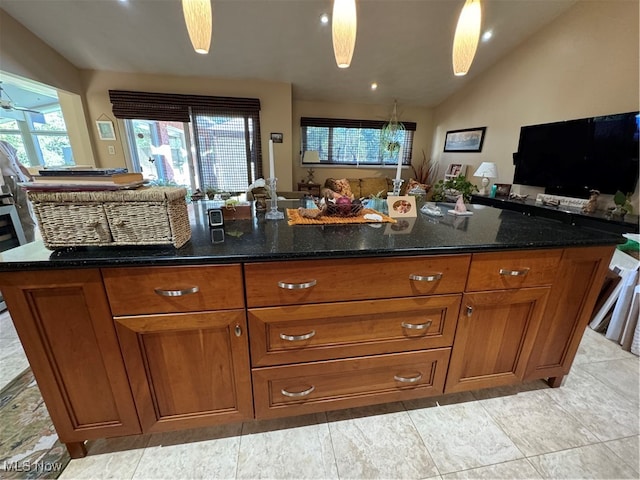 kitchen featuring open floor plan, brown cabinets, vaulted ceiling, and dark stone countertops