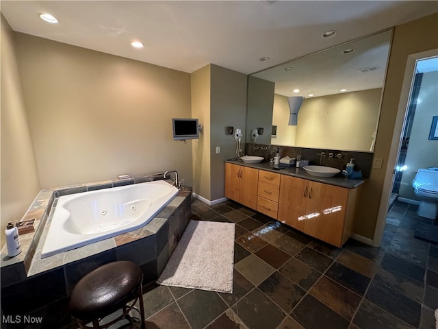 full bath with double vanity, toilet, a sink, a jetted tub, and baseboards