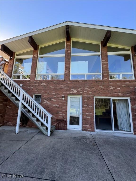 back of house featuring stairs and brick siding