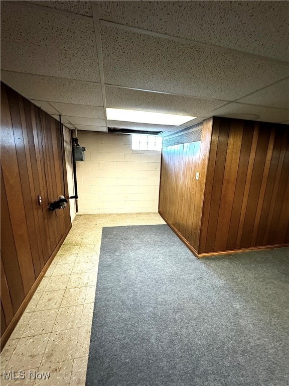 basement with a drop ceiling and wooden walls