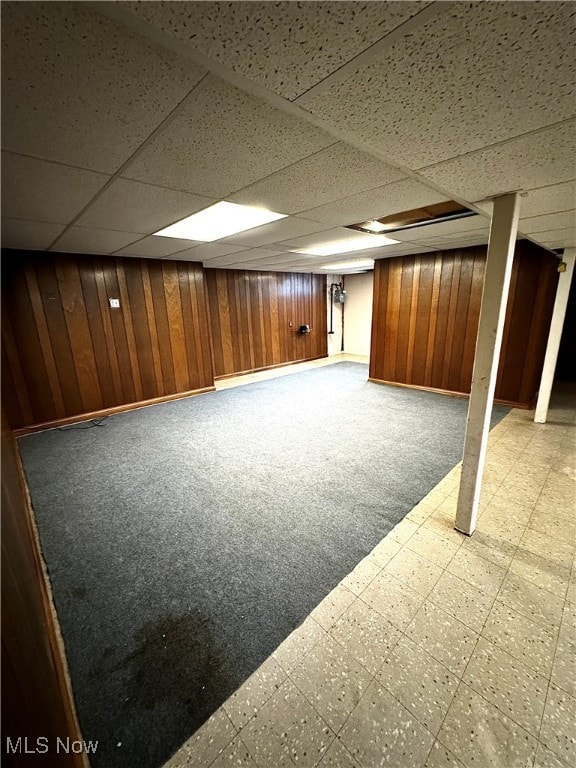 basement featuring a paneled ceiling and wooden walls