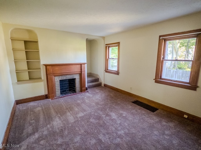 unfurnished living room featuring built in shelves, carpet floors, and a healthy amount of sunlight