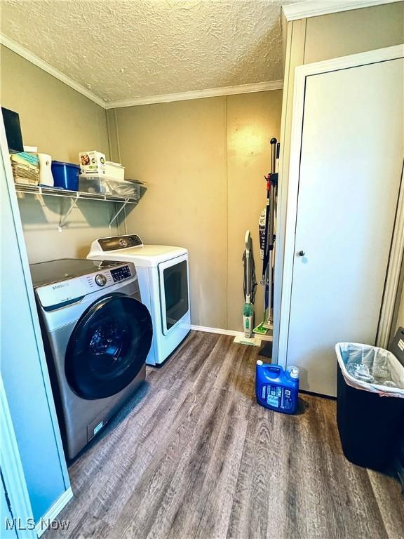 laundry room featuring dark wood-type flooring, washer and dryer, a textured ceiling, and ornamental molding