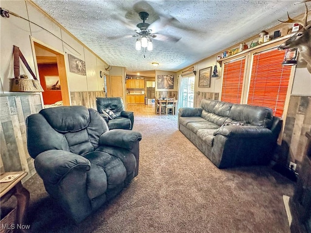 living room featuring ceiling fan, carpet floors, a textured ceiling, and wooden walls