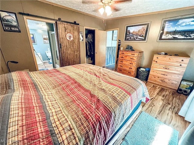 bedroom with hardwood / wood-style flooring, ceiling fan, a barn door, a textured ceiling, and a closet