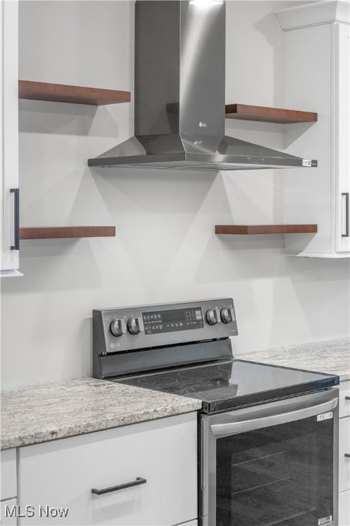 kitchen featuring white cabinets, stainless steel range with electric stovetop, and wall chimney range hood