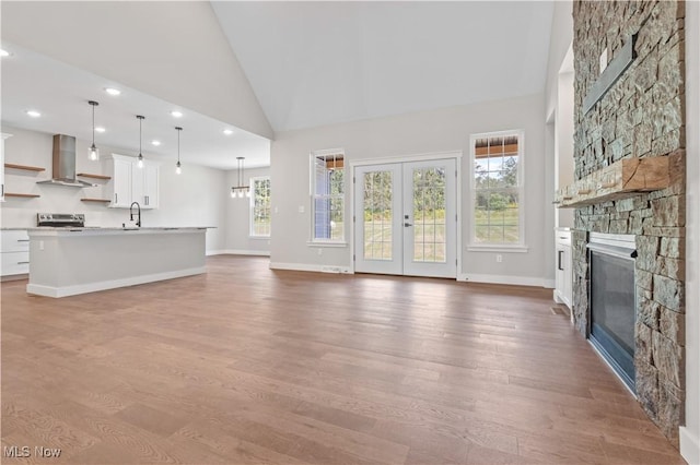 unfurnished living room with french doors, sink, high vaulted ceiling, wood-type flooring, and a fireplace