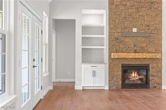 unfurnished living room with hardwood / wood-style floors, built in shelves, a wealth of natural light, and french doors