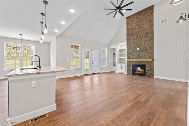 unfurnished living room with ceiling fan, sink, high vaulted ceiling, hardwood / wood-style floors, and a fireplace