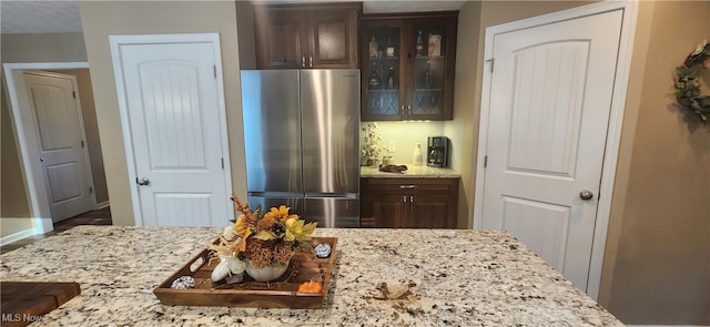 kitchen with dark brown cabinets, light stone countertops, and stainless steel refrigerator