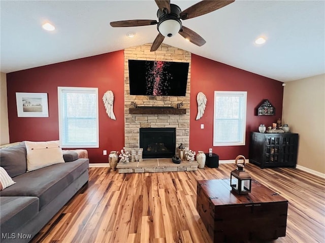 living room with wood-type flooring, vaulted ceiling, ceiling fan, and a fireplace