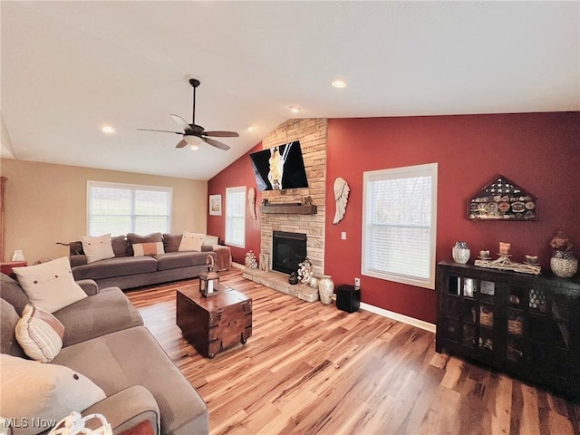 living room featuring hardwood / wood-style floors, a wealth of natural light, vaulted ceiling, and a stone fireplace