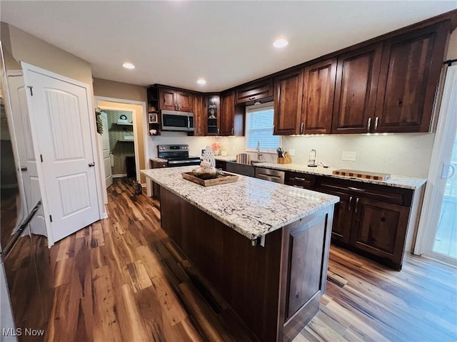 kitchen with stainless steel appliances, hardwood / wood-style flooring, a center island, and dark brown cabinetry