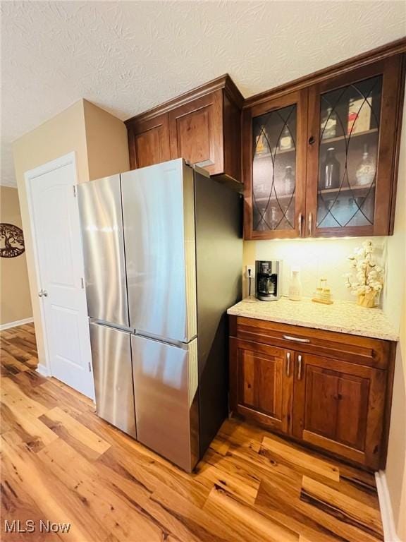 kitchen featuring stainless steel fridge, light stone countertops, a textured ceiling, and light wood-type flooring