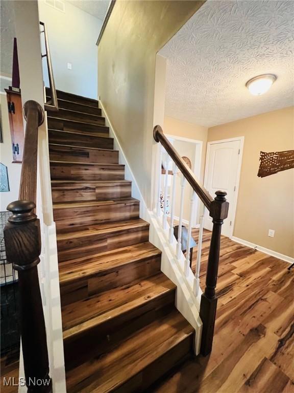 stairs with wood-type flooring and a textured ceiling