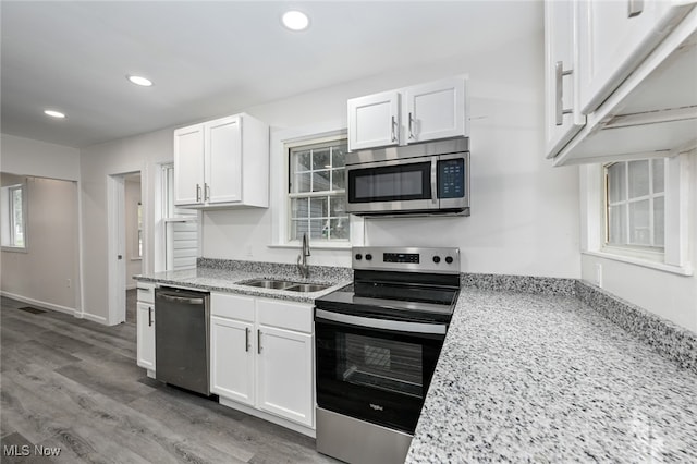 kitchen with white cabinets, light stone countertops, sink, appliances with stainless steel finishes, and light wood-type flooring