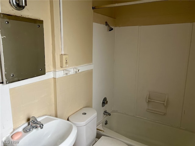 full bathroom featuring sink, tile walls, toilet, and shower / washtub combination