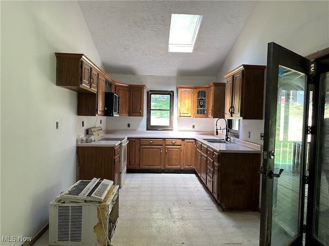 kitchen featuring a textured ceiling, electric range oven, lofted ceiling with skylight, and sink