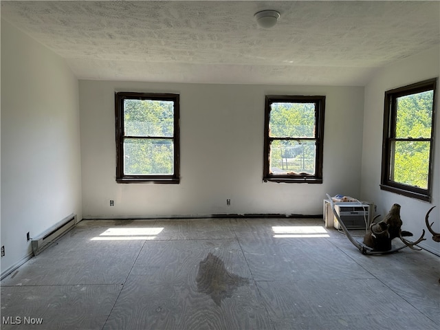 spare room featuring a textured ceiling, baseboard heating, a wall mounted air conditioner, and a wealth of natural light