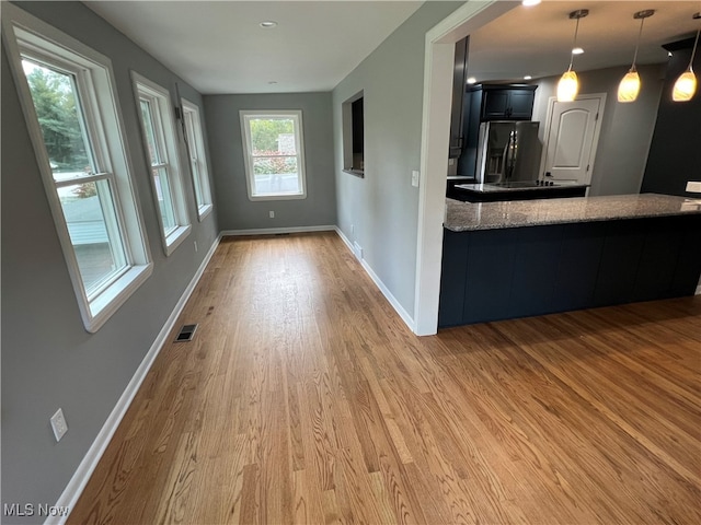 kitchen featuring hanging light fixtures, wood-type flooring, light stone counters, and stainless steel refrigerator with ice dispenser