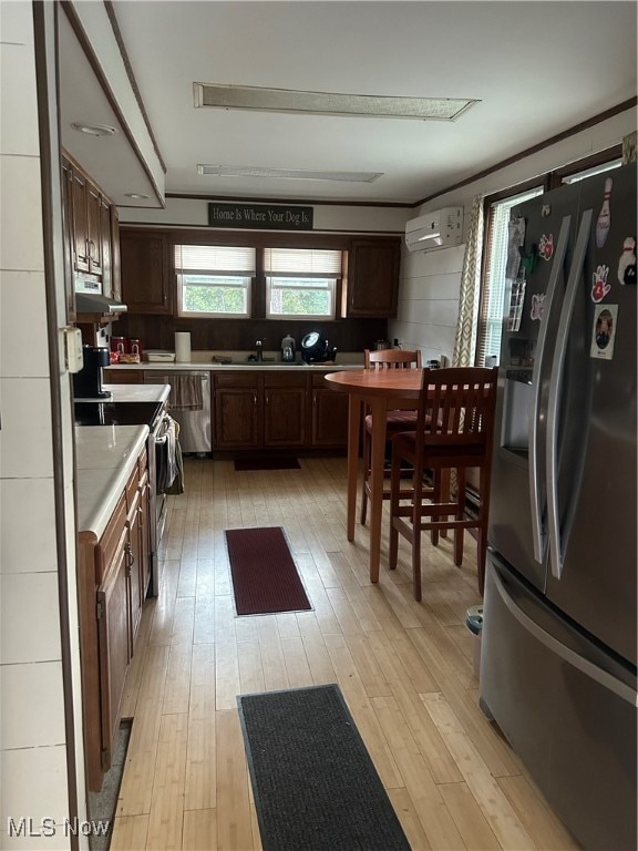 kitchen with stainless steel appliances, range hood, light hardwood / wood-style flooring, dark brown cabinetry, and a wall mounted air conditioner