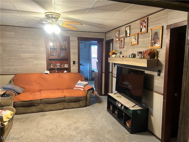 living room featuring carpet, a drop ceiling, wooden walls, and ceiling fan