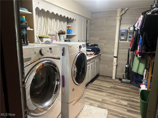 laundry area with light hardwood / wood-style floors, washing machine and dryer, and cabinets