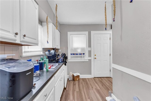 kitchen with plenty of natural light, light wood finished floors, backsplash, and white cabinets
