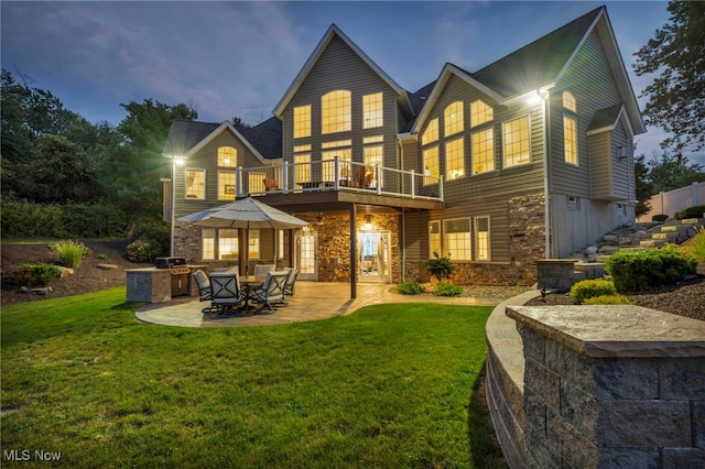 back house at dusk with a patio, a yard, and a balcony