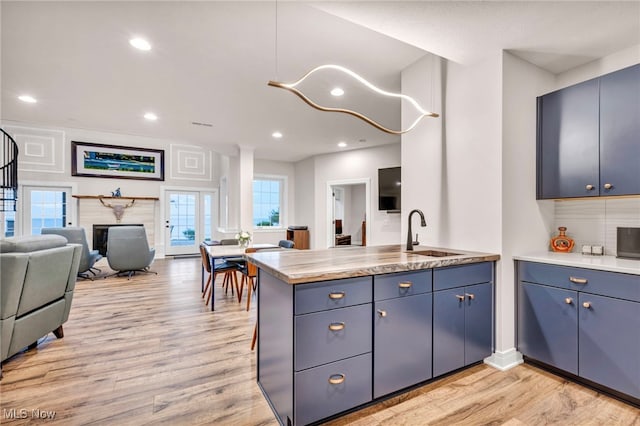 kitchen featuring light wood-type flooring, kitchen peninsula, sink, and blue cabinetry