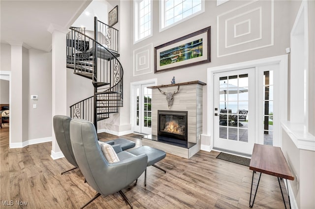 living room featuring wood-type flooring, a tiled fireplace, and a high ceiling