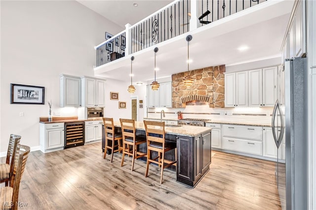 kitchen with stainless steel refrigerator, a center island with sink, beverage cooler, and a high ceiling