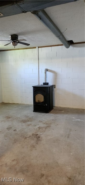 basement with a textured ceiling, ceiling fan, and a wood stove