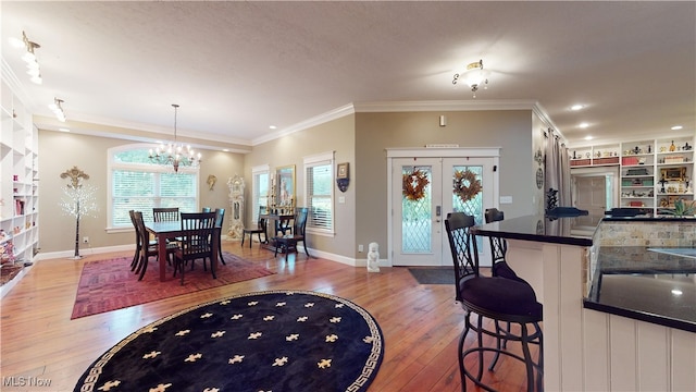 dining area featuring wood-type flooring, a notable chandelier, french doors, and ornamental molding