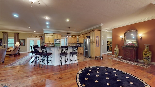 kitchen with light wood-type flooring, ornamental molding, hanging light fixtures, appliances with stainless steel finishes, and a kitchen bar