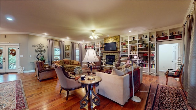 living room with crown molding, ceiling fan, a stone fireplace, and hardwood / wood-style floors