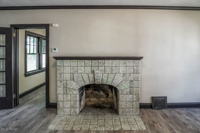 details with a textured ceiling, wood-type flooring, crown molding, and a tiled fireplace