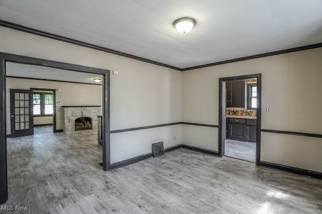 spare room featuring light wood-type flooring, a healthy amount of sunlight, a fireplace, and crown molding