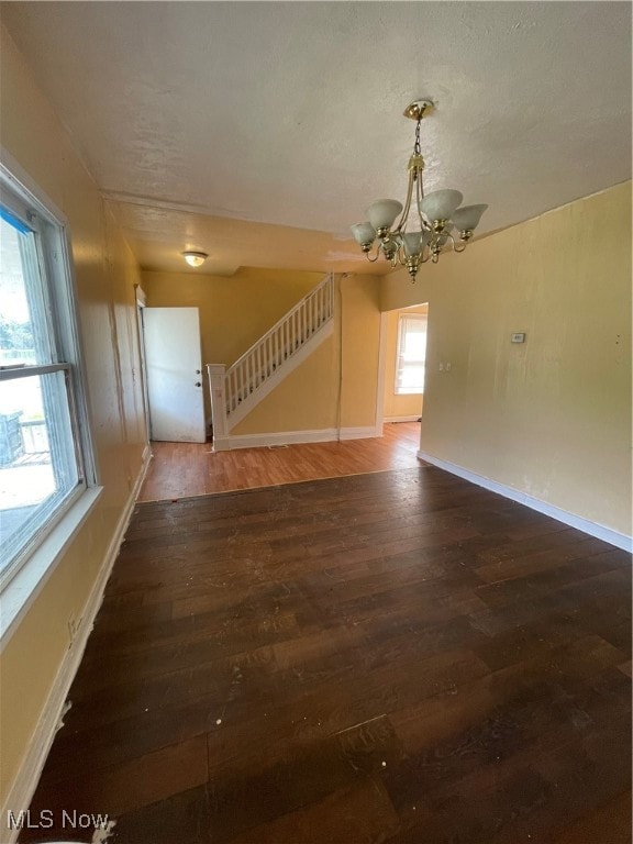 empty room featuring a notable chandelier, dark wood-type flooring, and a healthy amount of sunlight